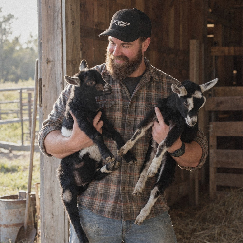 Andrew Pignato in an Afternoon Farmer hat holding two baby goats in the barn